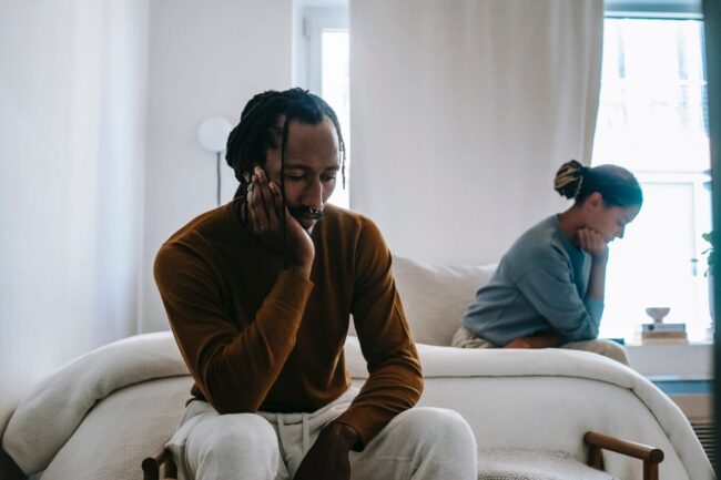 A man sitting on top of a couch next to another person. A man sitting on top of a couch next to another person.