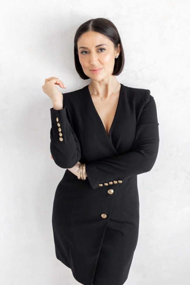 A woman in black suit standing next to wall.