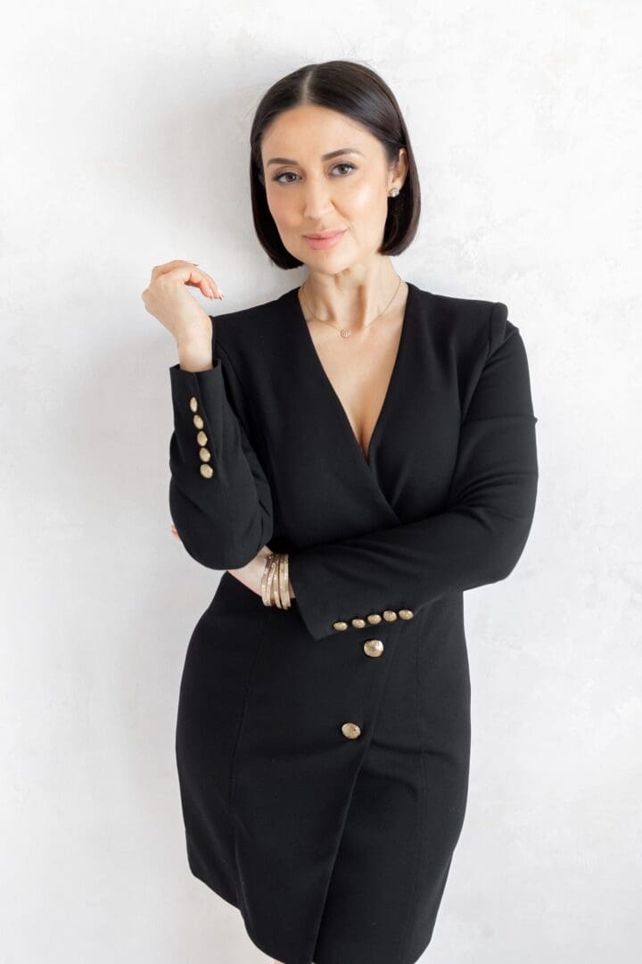 A woman in black suit standing next to wall.